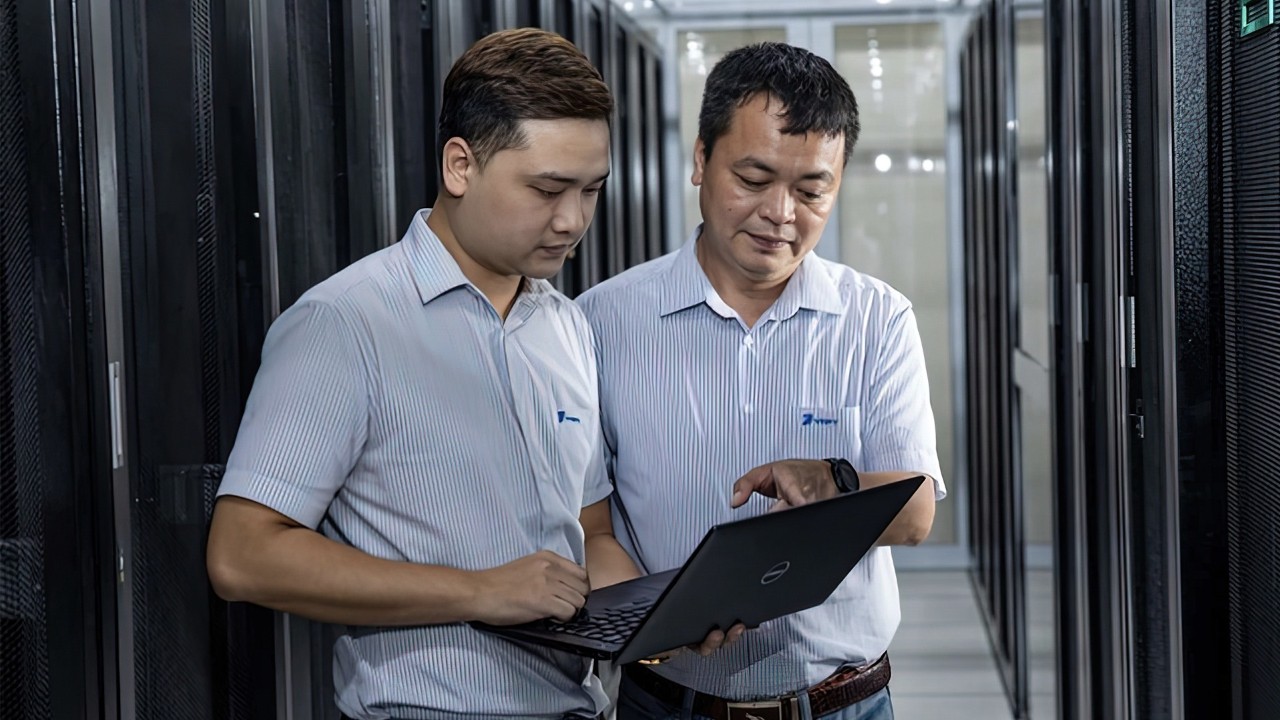 Two men standing in front of a server, discussing technical details.