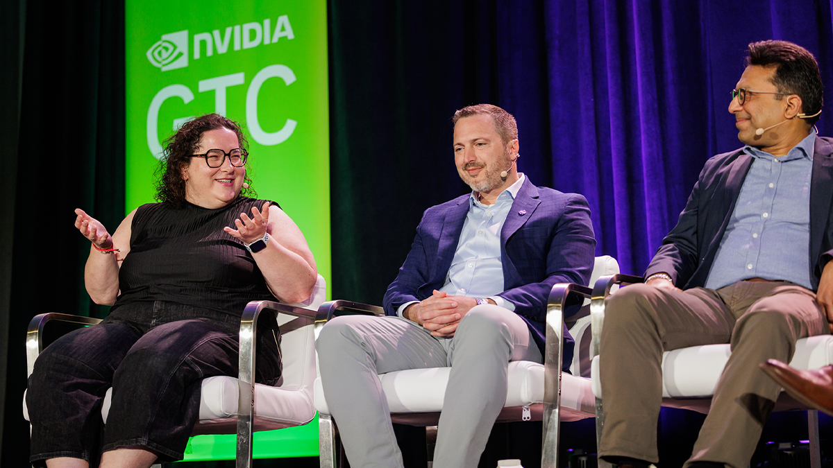 Three panelists sit onstage at an NVIDIA GTC event, talking and smiling.