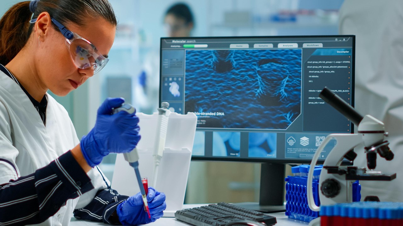 Uno scienziato in camice da laboratorio che lavora intensamente su un computer, conducendo esperimenti in una struttura di ricerca.