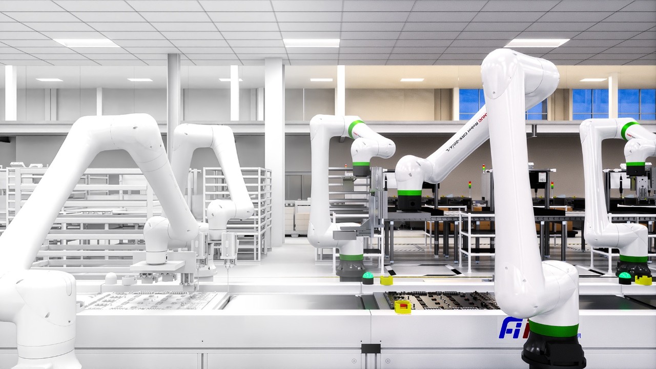 White robotic arms are positioned over a production line with circuit boards in a factory.